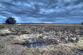 Abandoned barn in mud field HDR photo with cloudy sky