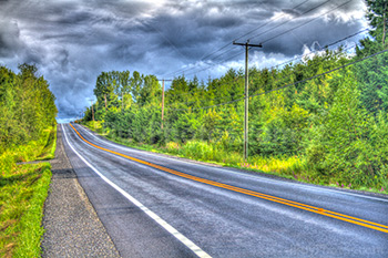 Route asplatée de campagne avec abres et ciel orageux en HDR