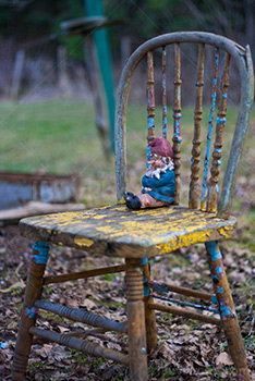 Garden gnome seating on old chair among leaves