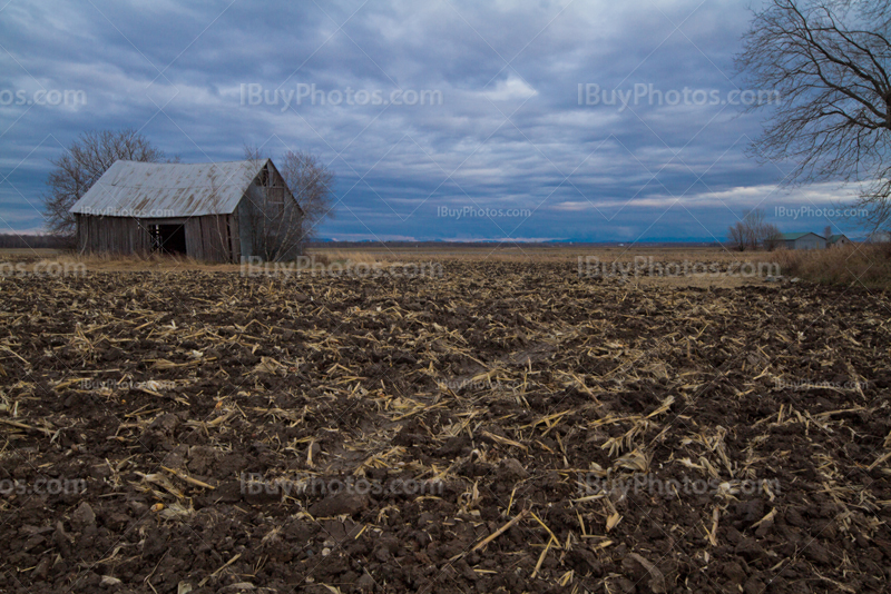 Abandoned barn in mud field under cloudy sky