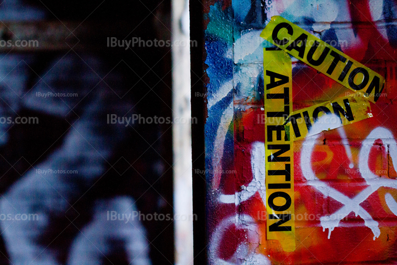 Yellow caution tape on wall covered by graffiti beside doorway