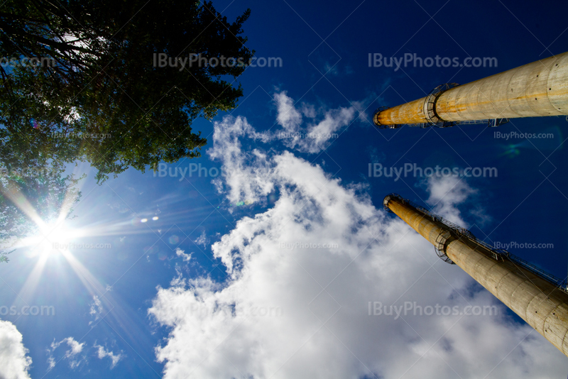 Cheminées d'usine avec soleil dans ciel avec nuages