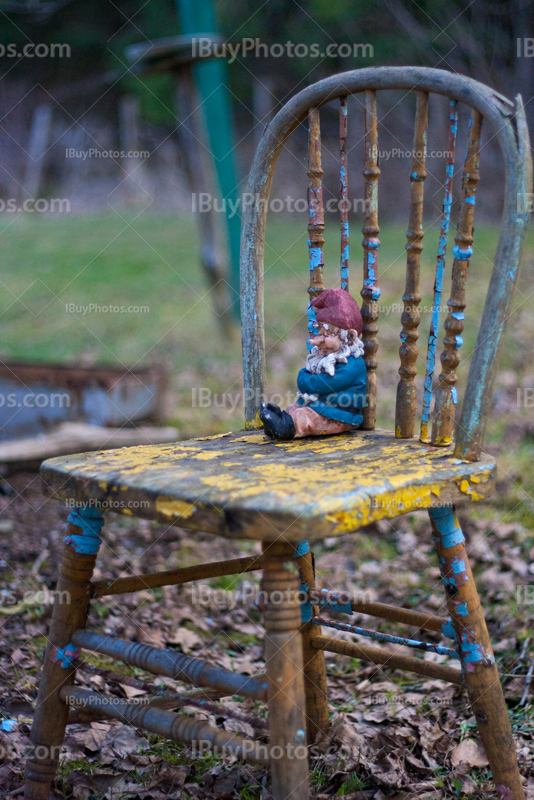 Garden gnome seating on old chair among leaves