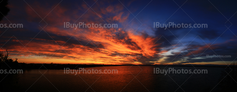 Panoramic photo of sunset over a pond with blue, red and orange sky with clouds