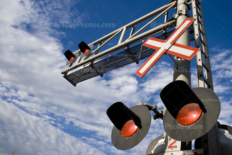 Railway crossing signals and lights at barrier with cloudy sky