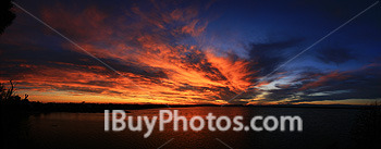 Panoramic photo of sunset over a pond with blue, red and orange sky with clouds