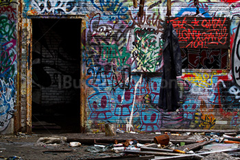 Dirty black coat hanging in abandoned building, graffiti and spray cans