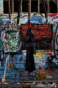Black coat hanging in abandoned building with graffiti on wall